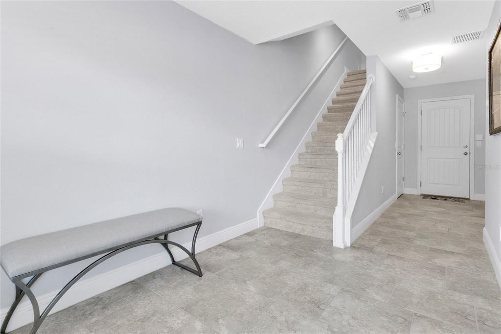 A foyer features a grey bench, tiled flooring, and a carpeted staircase with white railings — 10534 GREEN IVY LANE, ORLANDO, FL