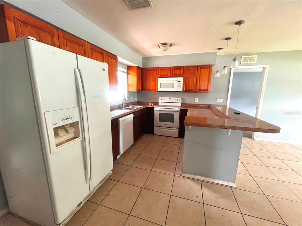 A kitchen features wood cabinets, white appliances, tile flooring, and a raised breakfast bar — 731 LAKESIDE DRIVE, LARGO, FL