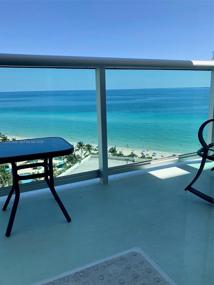 A balcony with a table and chairs overlooks the ocean and a sandy beach — 3901 S Ocean Dr # 14Z, Hollywood FL 33019, HOLLYWOOD, FL