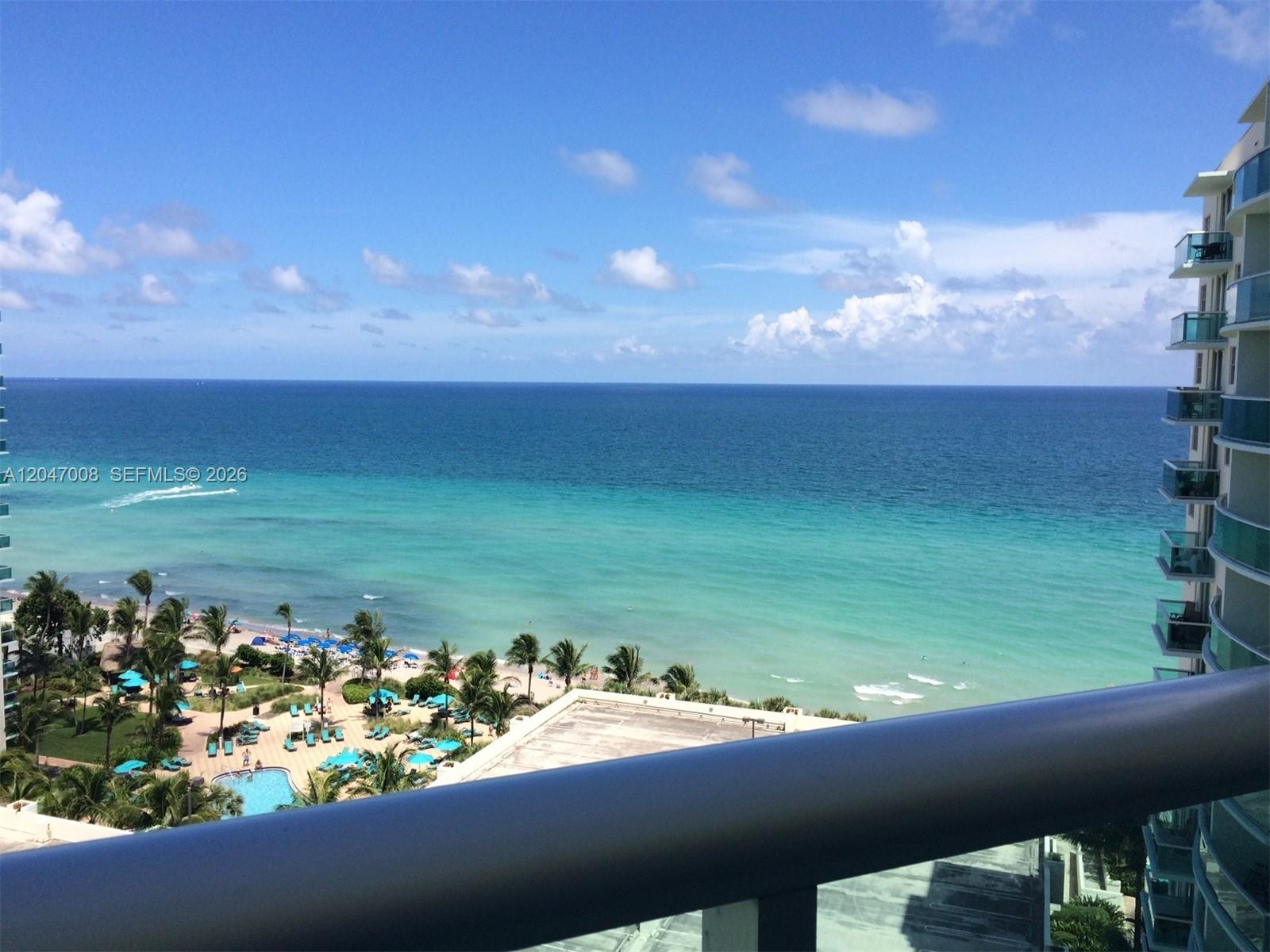 A high-angle view of a beach and ocean from a balcony with a glass railing — 3901 S Ocean Dr # 14Z, Hollywood FL 33019, HOLLYWOOD, FL