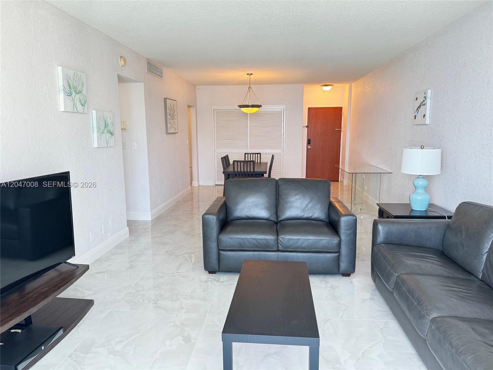 A living room features white tiled floors, dark leather sofas, and a dining area beyond — 3901 S Ocean Dr # 14Z, Hollywood FL 33019, HOLLYWOOD, FL
