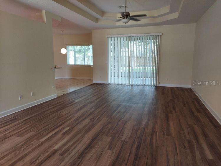 A living room with wood-look flooring, a tray ceiling, and sliding glass doors — 3 WAINMONT PLACE, PALM COAST, FL