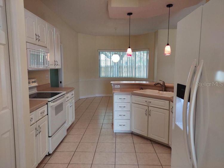 A kitchen features white cabinets, tile flooring, a white stove, and two hanging pendant lights — 3 WAINMONT PLACE, PALM COAST, FL