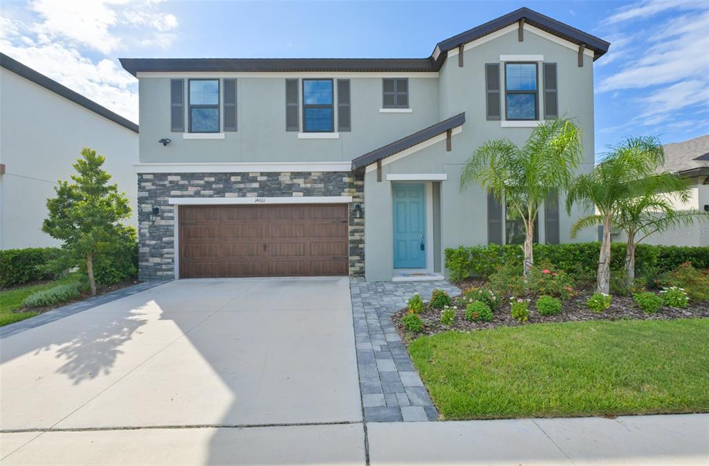 A two-story house features a light green exterior, stone accents, a garage, and palm trees — 14661 HORSE TROT ROAD, LITHIA, FL