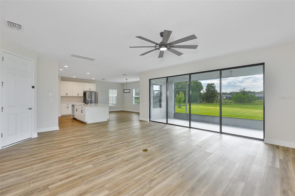 An open-concept living area features light wood-look flooring, a ceiling fan, and sliding glass doors — 14661 HORSE TROT ROAD, LITHIA, FL