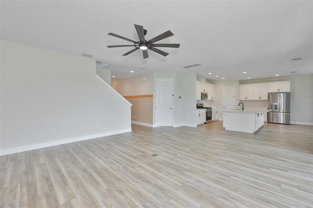An open-concept living area features light wood-look flooring, a ceiling fan, and a white kitchen — 14661 HORSE TROT ROAD, LITHIA, FL