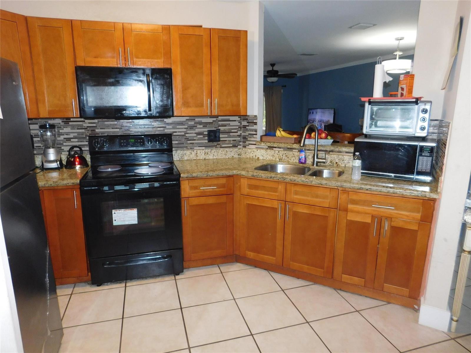 A kitchen features wood cabinets, granite countertops, black appliances, and a tiled floor — 1106 SW 44th Way, Deerfield Beach FL 33442, DEERFIELD BEACH, FL