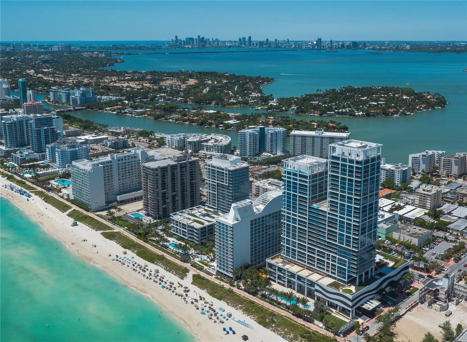 An aerial view shows high-rise beachfront condominiums along a turquoise coastline with a city skyline — 6899 Collins Ave # 1610, Miami Beach FL 33141, MIAMI BEACH, FL