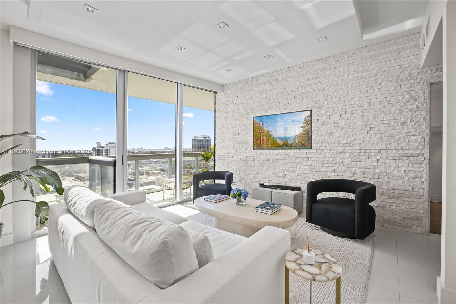 A modern living room features a white stone accent wall, floor-to-ceiling windows, and balcony views — 6899 Collins Ave # 1610, Miami Beach FL 33141, MIAMI BEACH, FL
