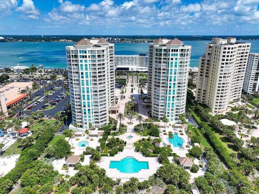 An aerial view of three high-rise residential buildings with pools and landscaped grounds near water — 1180 GULF BLVD UNIT 504, CLEARWATER BEACH, FL