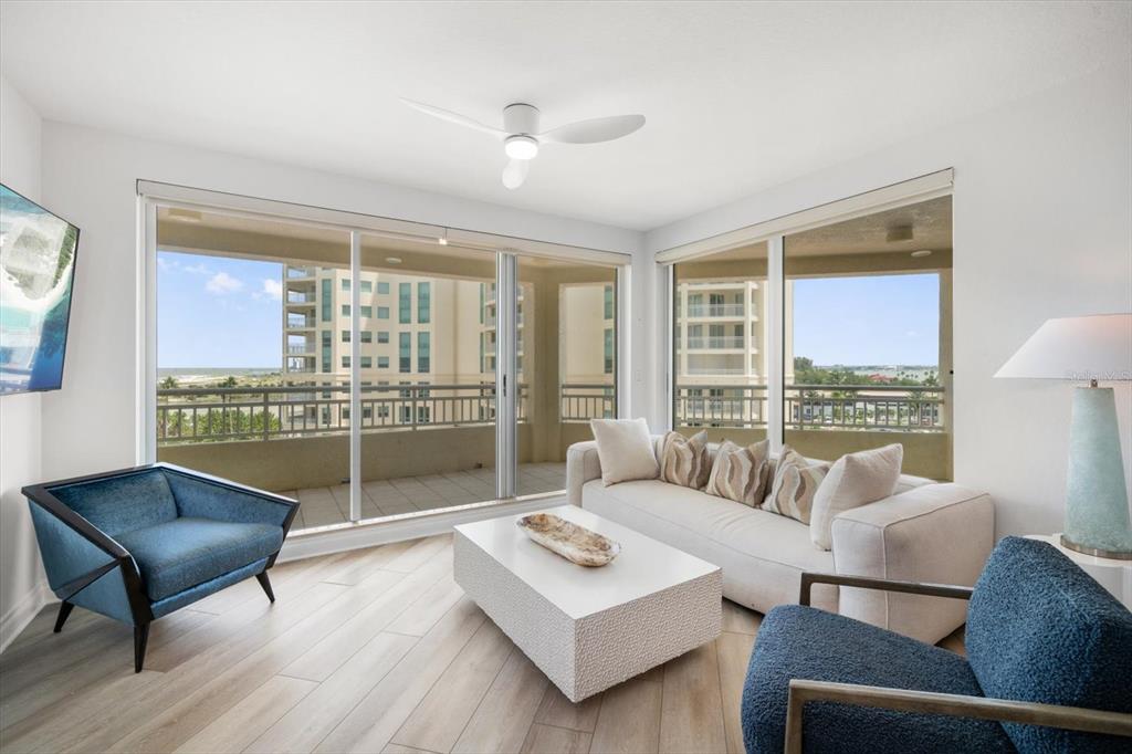 A living room features a white sofa, two blue armchairs, and floor-to-ceiling balcony windows — 1180 GULF BLVD UNIT 504, CLEARWATER BEACH, FL