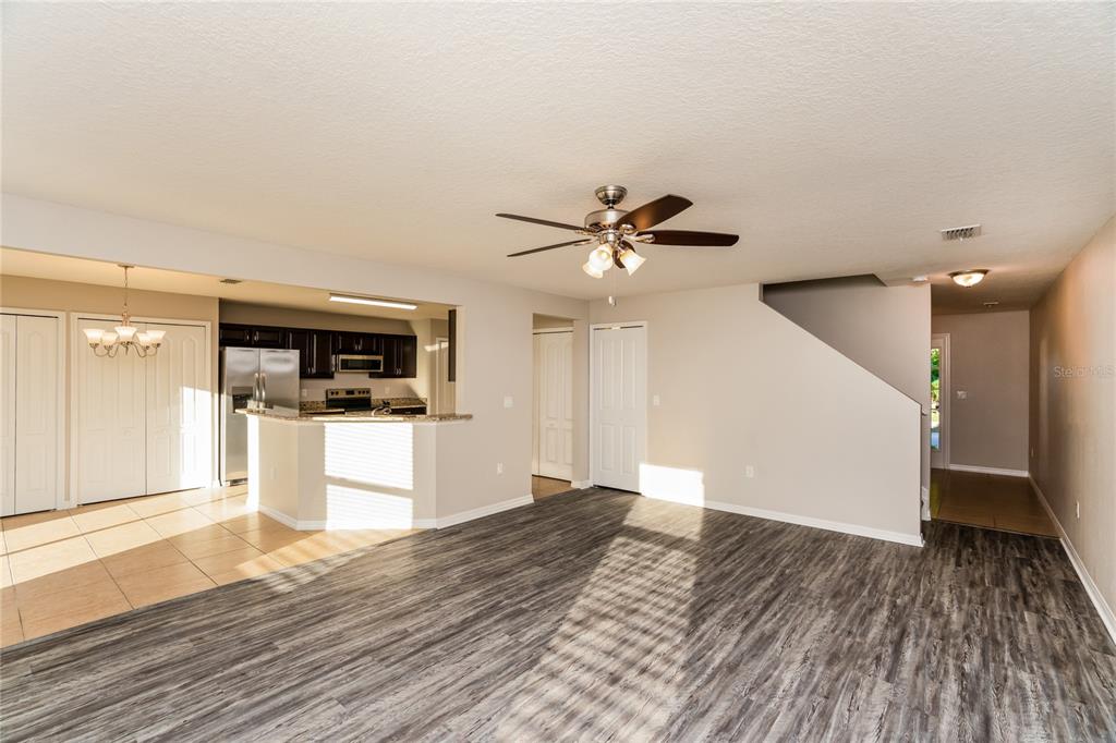 A living room with wood-look flooring opens to a kitchen with dark cabinets and tile — 13307 WATERFORD CASTLE DRIVE, DADE CITY, FL
