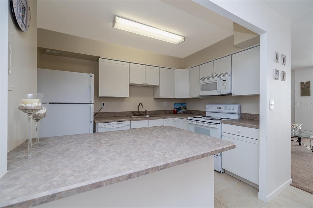 A kitchen features white cabinets, laminate countertops, a white refrigerator, and a white electric stove — 2800 N ATLANTIC AVENUE UNIT 511, DAYTONA BEACH, FL