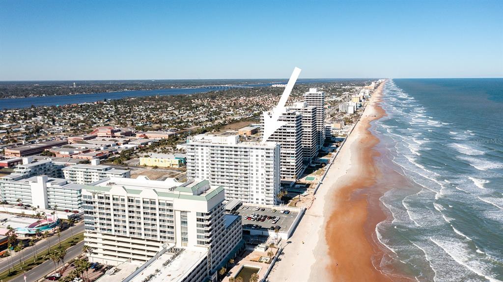 An aerial view shows a tall beachfront condominium building with a white arrow pointing down — 2800 N ATLANTIC AVENUE UNIT 511, DAYTONA BEACH, FL