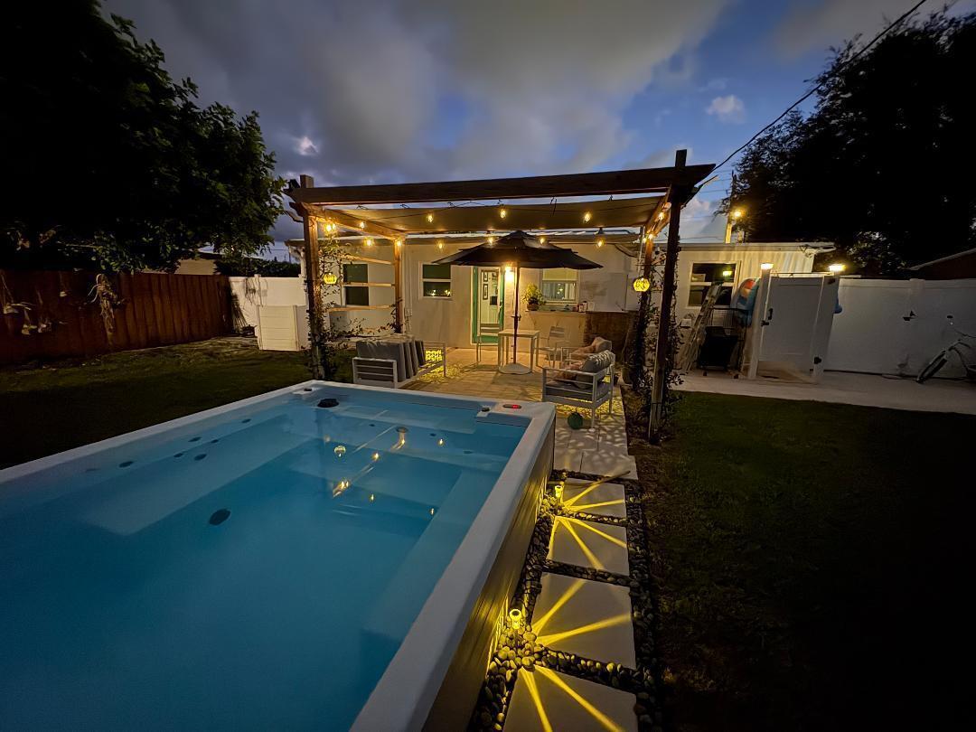 A backyard at dusk features a rectangular swim spa, a wooden pergola, and stone pavers — 127 SW 10th Avenue, Boynton Beach FL 33435, BOYNTON BEACH, FL