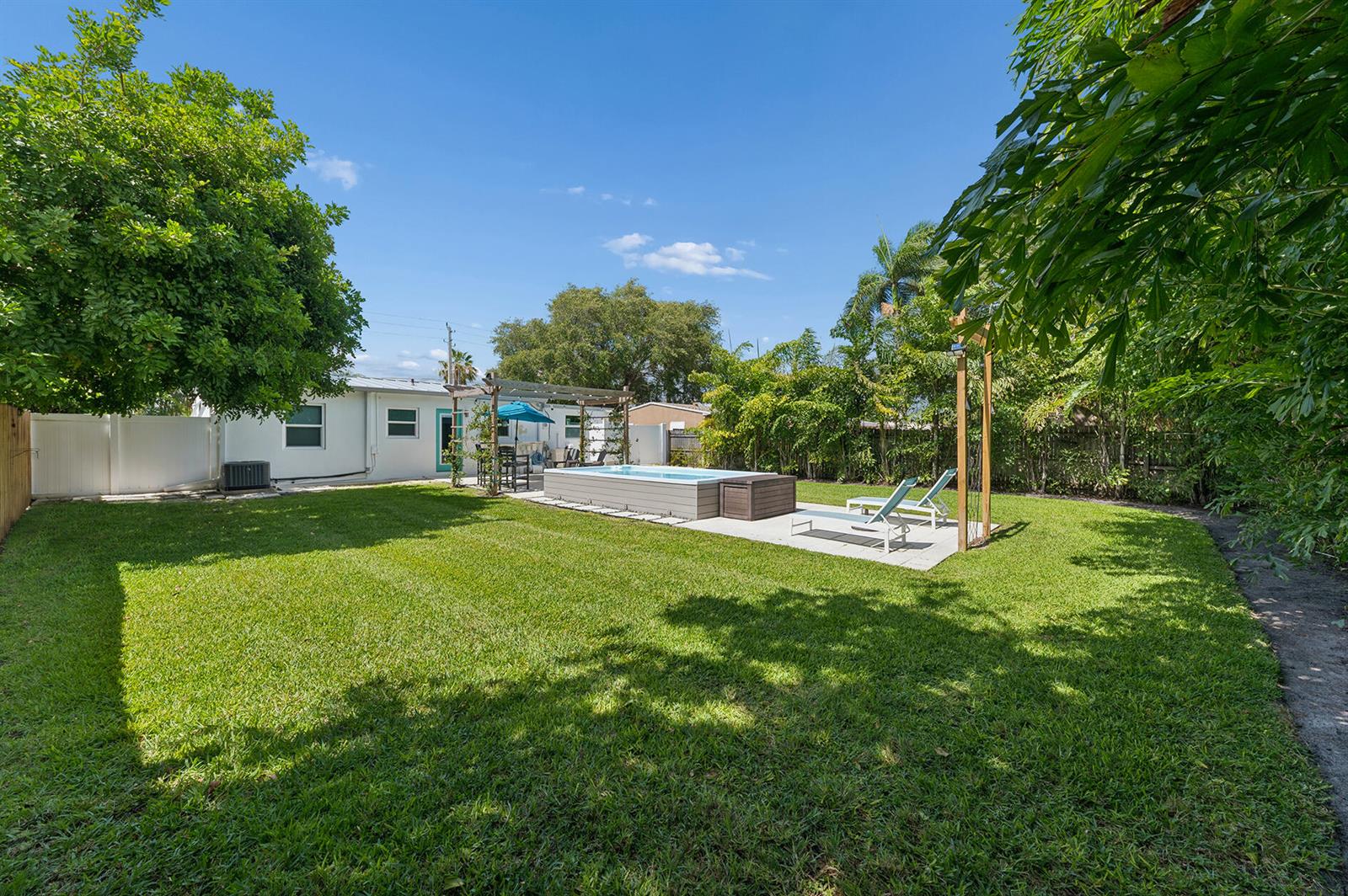 A backyard features a rectangular above-ground pool, a patio with lounge chairs, and lush landscaping — 127 SW 10th Avenue, Boynton Beach FL 33435, BOYNTON BEACH, FL
