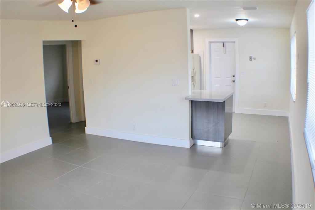 An interior view shows a living area with gray tile flooring and a kitchen peninsula — 719 SW 7th Street # 2, Hallandale Beach FL 33009, HALLANDALE BEACH, FL