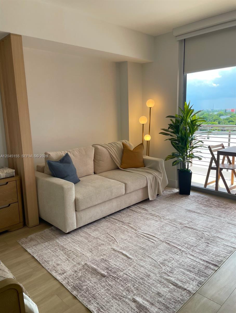 A living room features a beige sofa, a patterned rug, and a balcony with outdoor seating — 90 NE 32 # 819, Miami FL 33137, MIAMI, FL