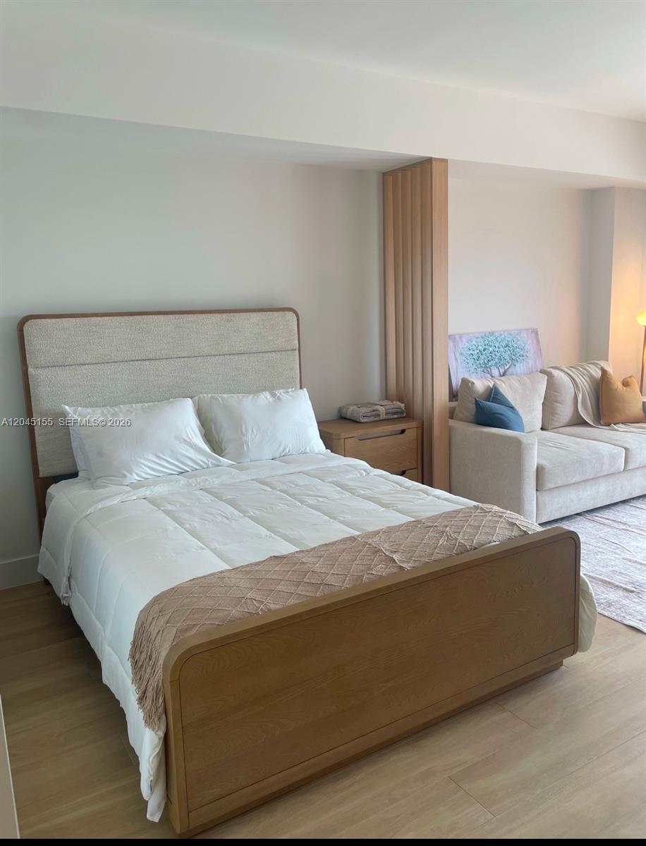 A bedroom features a wooden bed frame, upholstered headboard, and an adjacent living area — 90 NE 32 # 819, Miami FL 33137, MIAMI, FL