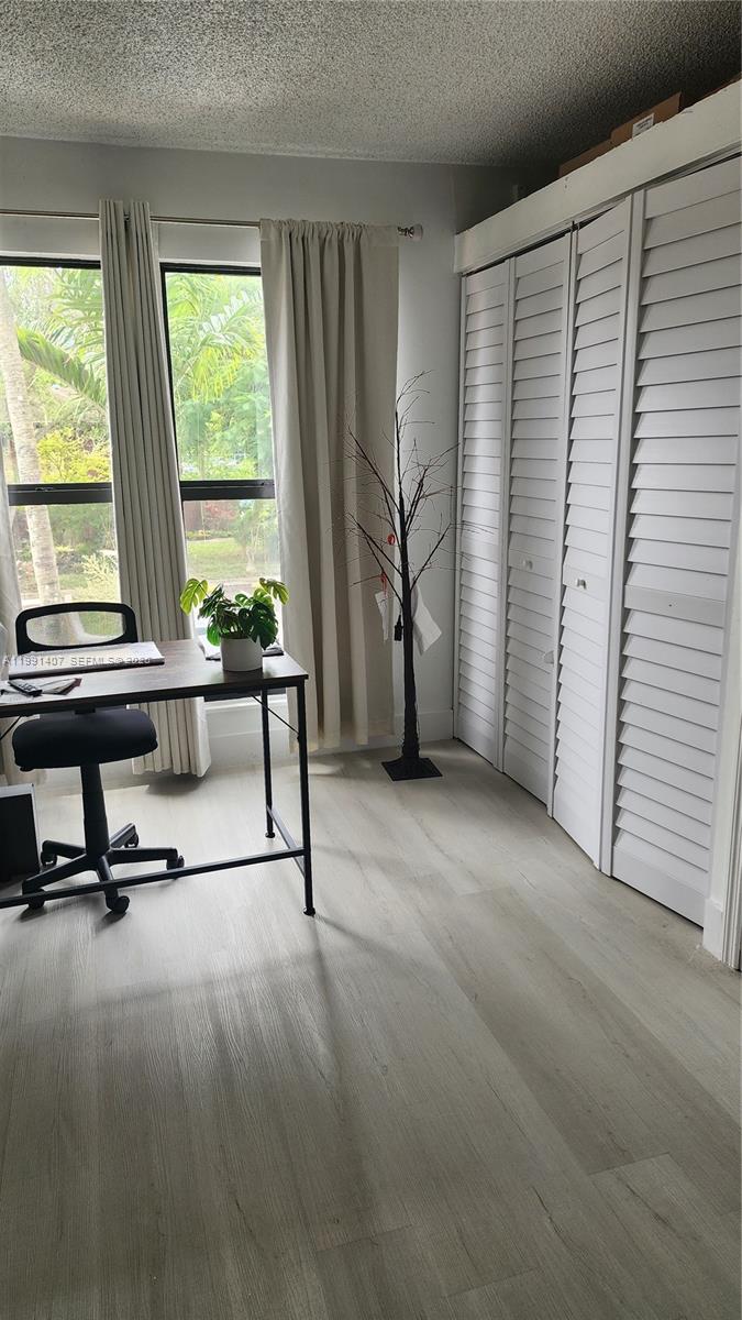 A home office features light wood-look flooring, a desk, a decorative tree, and louvered closet doors — 6231 SW 116th Pl # C, Miami FL 33173, MIAMI, FL