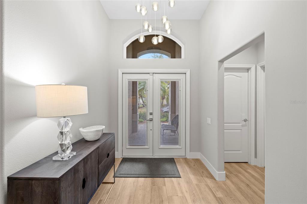 A bright entryway features a dark wood console table, a modern chandelier, and double glass doors — 8322 WHISPERING WOODS COURT, BRADENTON, FL