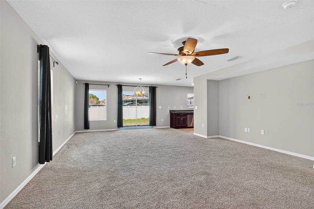 A spacious living room features beige carpeting, neutral walls, a ceiling fan, and sliding glass doors — 10405 LAGUNA PLAINS DRIVE, RIVERVIEW, FL