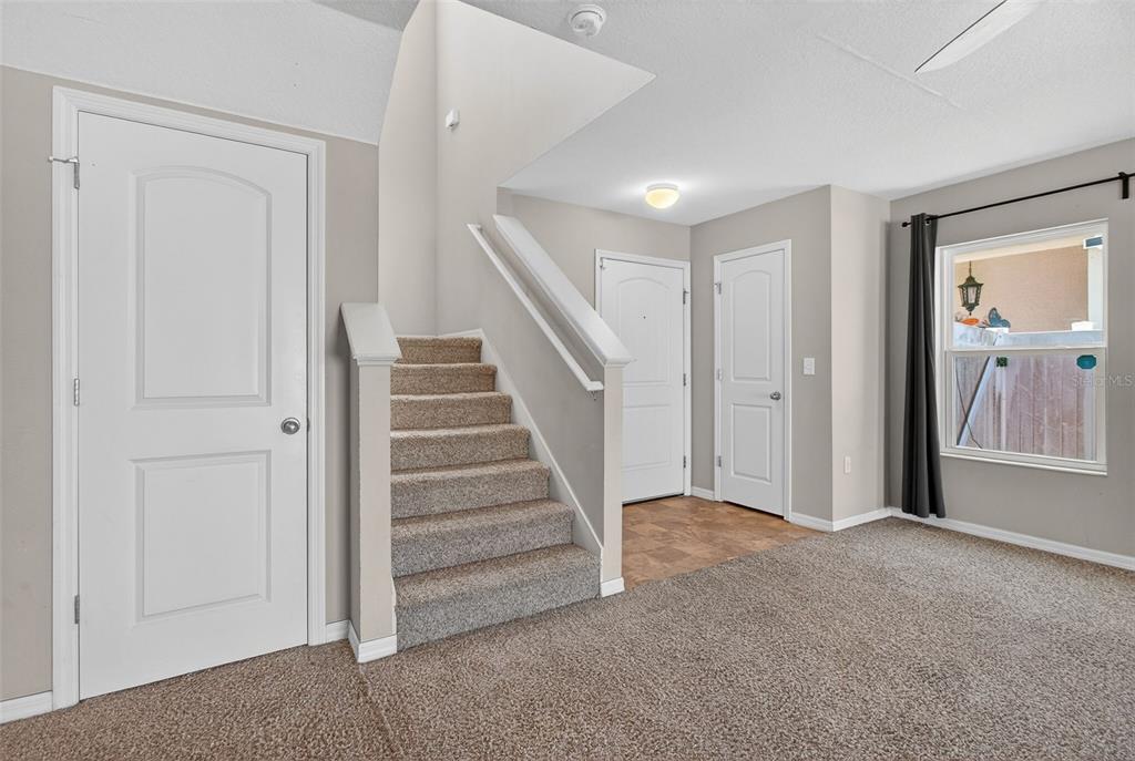 A carpeted room features a staircase, a front door, and a window with dark curtains — 10405 LAGUNA PLAINS DRIVE, RIVERVIEW, FL
