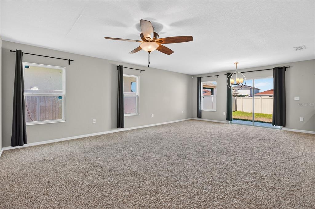 A spacious living room features beige carpeting, gray walls, a ceiling fan, and sliding glass doors — 10405 LAGUNA PLAINS DRIVE, RIVERVIEW, FL