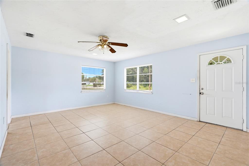 A living room with light blue walls, beige tile flooring, two windows, and a ceiling fan — 701 59TH STREET S, GULFPORT, FL