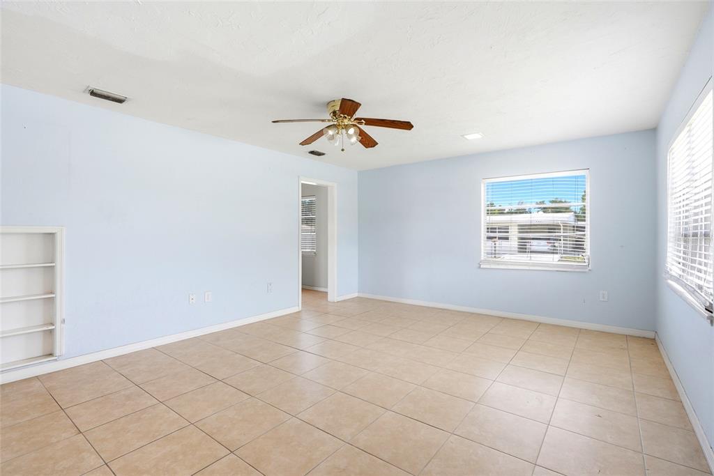 An empty room with light blue walls, beige tile flooring, a ceiling fan, and windows — 701 59TH STREET S, GULFPORT, FL