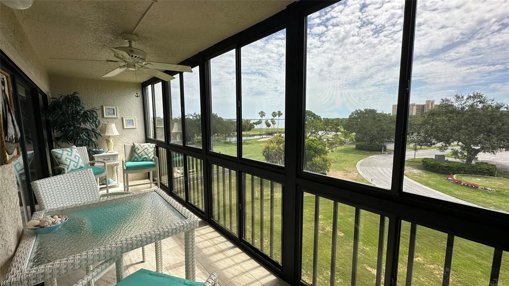 A screened-in balcony features wicker furniture and views of a golf course and water — 3400 COVE CAY DRIVE UNIT 4E, CLEARWATER, FL