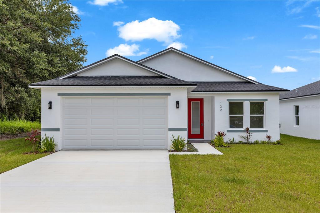 A single-story white house with a red front door, two-car garage, and a concrete driveway — 132 11TH AVENUE, OSTEEN, FL