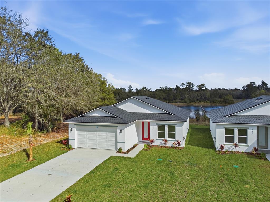 An exterior view of a modern white single-story house with a red front door — 132 11TH AVENUE, OSTEEN, FL