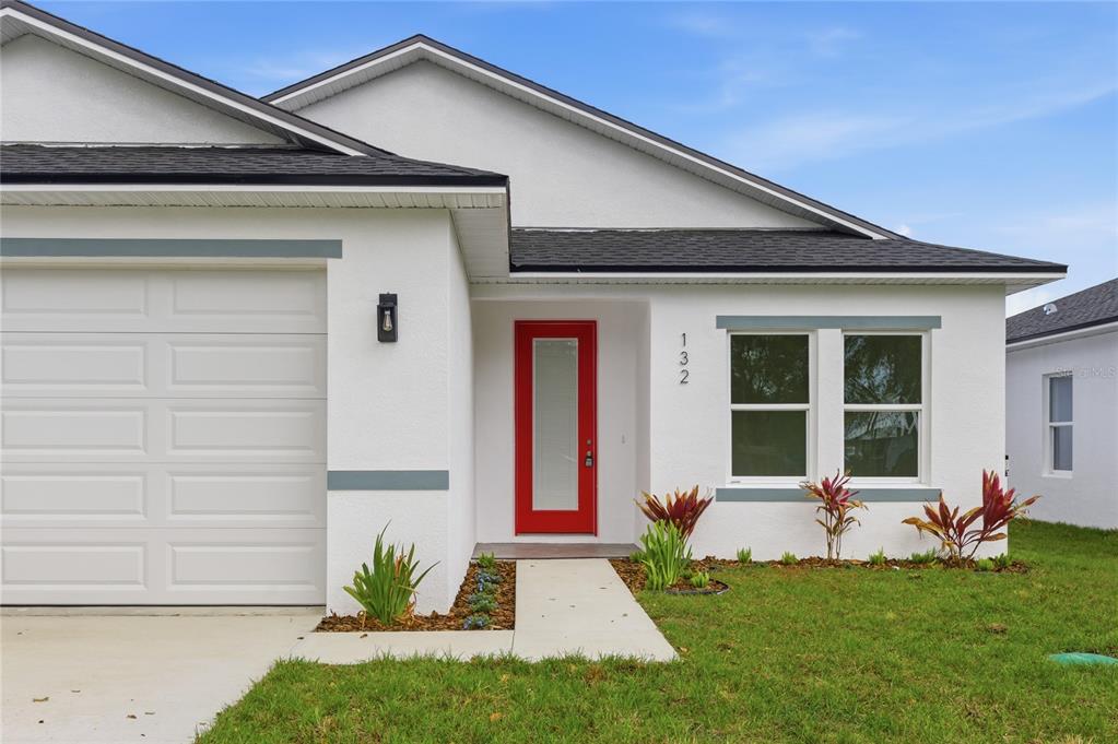 A white house exterior features a red front door, a garage, and a small lawn — 132 11TH AVENUE, OSTEEN, FL