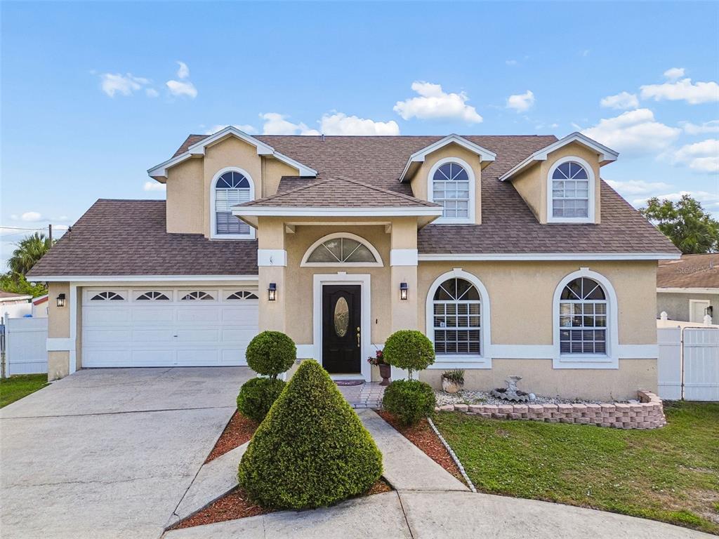 A two-story tan stucco house features a brown shingled roof, arched windows, and a garage — 10735 SE DRUMMOND ROAD, TAMPA, FL
