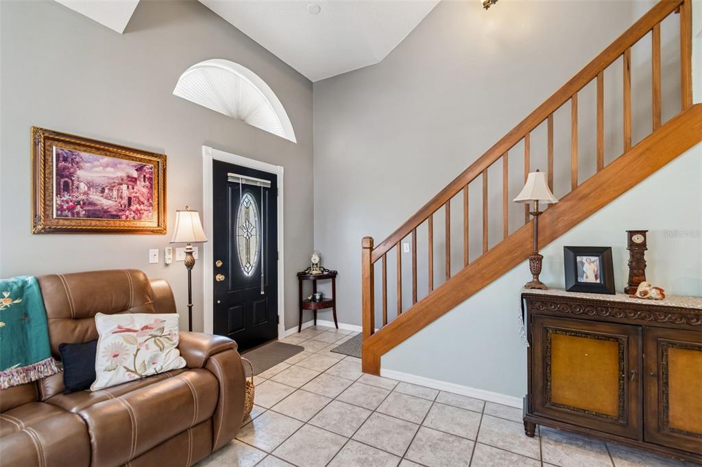An entryway features a tiled floor, a wooden staircase, a black front door, and furniture — 10735 SE DRUMMOND ROAD, TAMPA, FL