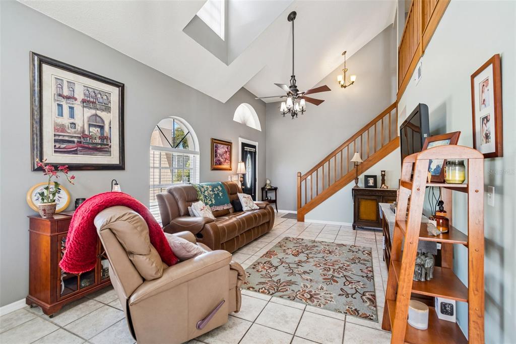 A living room with tile floors, a vaulted ceiling, a staircase, and a brown sofa — 10735 SE DRUMMOND ROAD, TAMPA, FL