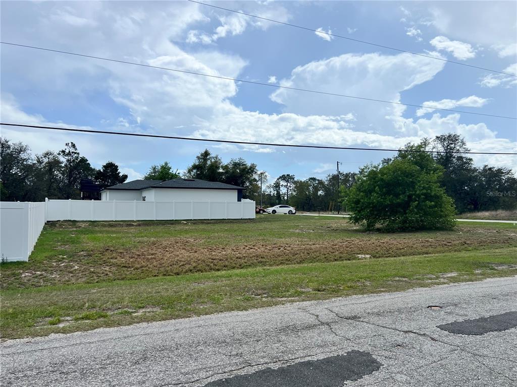 A vacant, grassy residential lot is bordered by a white vinyl fence and a road — 1337 HILLSBOROUGH DRIVE, POINCIANA, FL