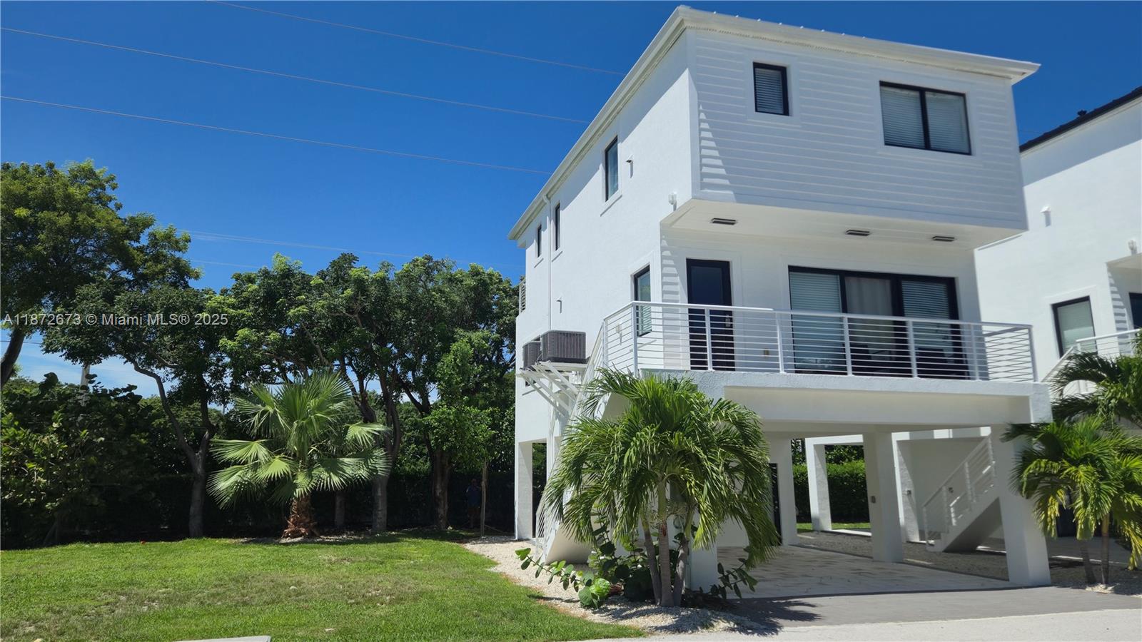 A white three-story stilt house features a balcony, ground-level parking, and surrounding palm trees — 94825 Overseas Hwy #281, Key Largo FL 33037, KEY LARGO, FL