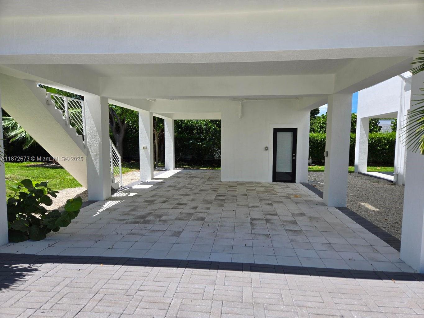 A covered ground-level patio features light-colored square tiles, white support columns, and an exterior staircase — 94825 Overseas Hwy #281, Key Largo FL 33037, KEY LARGO, FL