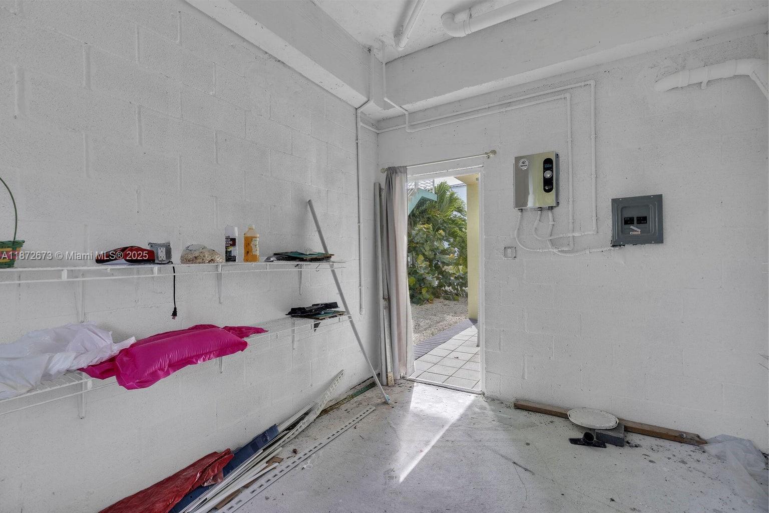 An unfinished utility room features white painted block walls, wire shelving, and an exterior door — 94825 Overseas Hwy #281, Key Largo FL 33037, KEY LARGO, FL