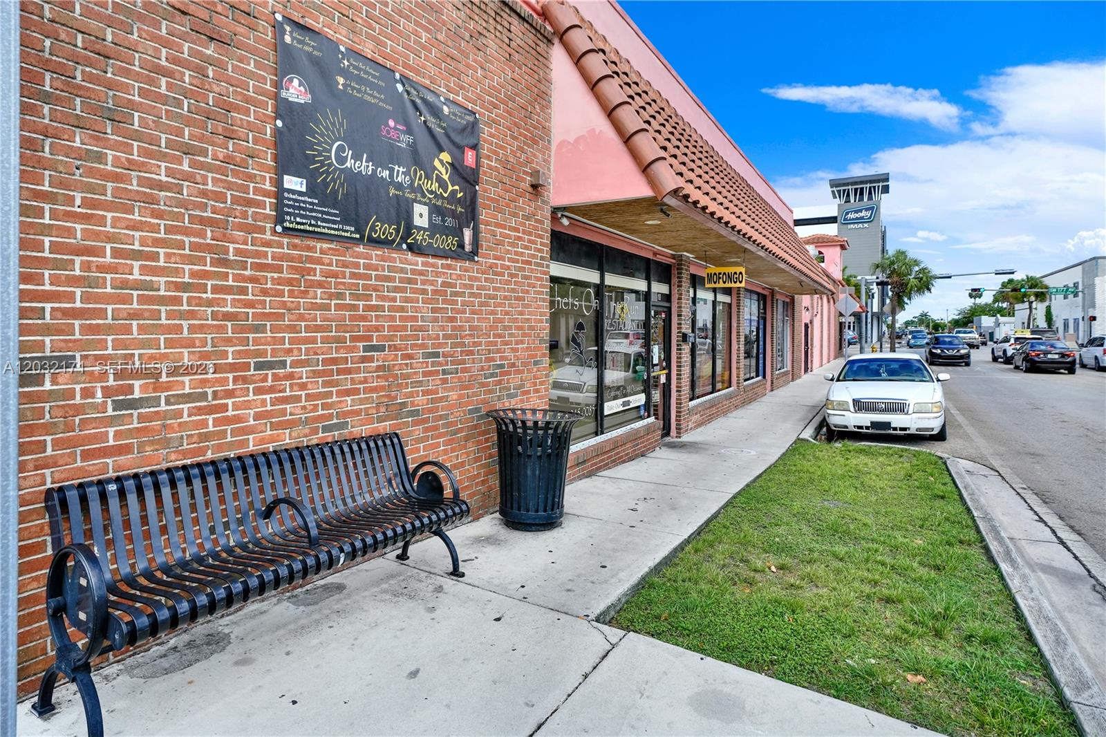 A brick building exterior features a restaurant entrance, a metal bench, and a trash can — 1 S Krome Ave, Homestead FL 33030, HOMESTEAD, FL