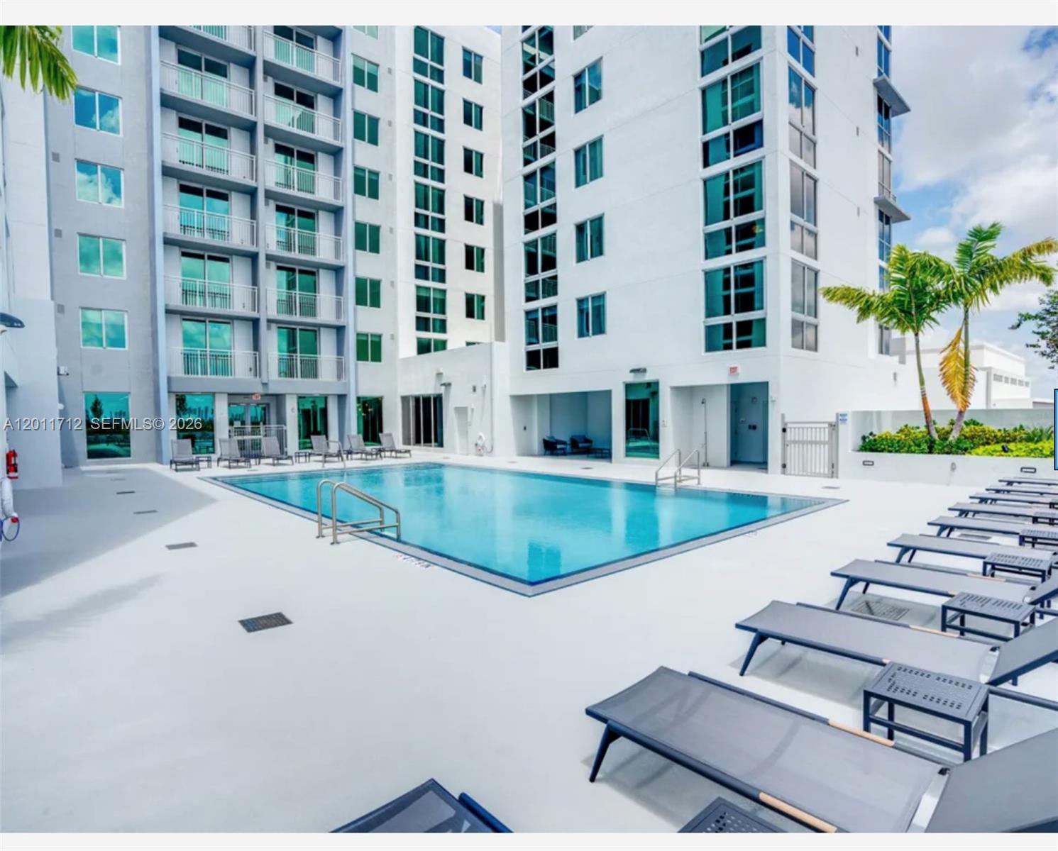 A rectangular swimming pool sits on a concrete deck surrounded by modern high-rise apartment buildings — 61 NW 37th Ave # 21, Miami FL 33125, MIAMI, FL