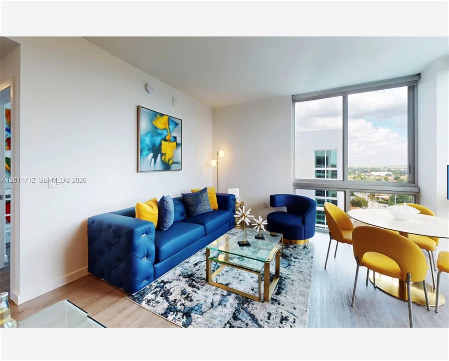 A living and dining area features a blue sofa, glass coffee table, and yellow chairs — 61 NW 37th Ave # 21, Miami FL 33125, MIAMI, FL