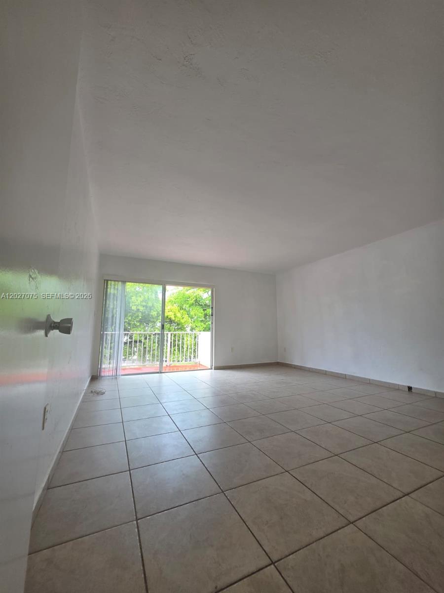 An empty room features white walls, light-colored floor tiles, and a sliding glass door — 1175 Normandy Dr # 3B, Miami Beach FL 33141, MIAMI BEACH, FL