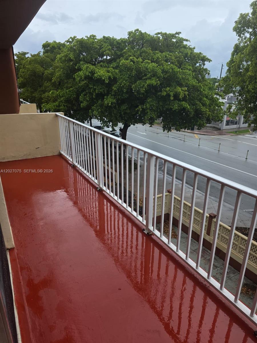 A red-painted balcony with a white metal railing overlooks a street and trees — 1175 Normandy Dr # 3B, Miami Beach FL 33141, MIAMI BEACH, FL