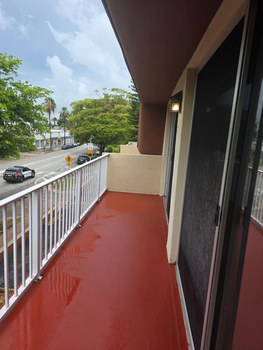 An outdoor balcony with a red floor, white metal railing, and a view of the street — 1175 Normandy Dr # 3B, Miami Beach FL 33141, MIAMI BEACH, FL