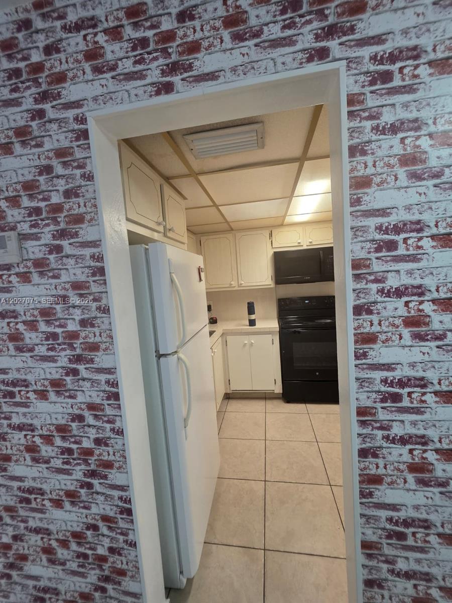 A kitchen with white cabinets and black appliances is viewed through a doorway with brick-patterned wallpaper — 1175 Normandy Dr # 3B, Miami Beach FL 33141, MIAMI BEACH, FL