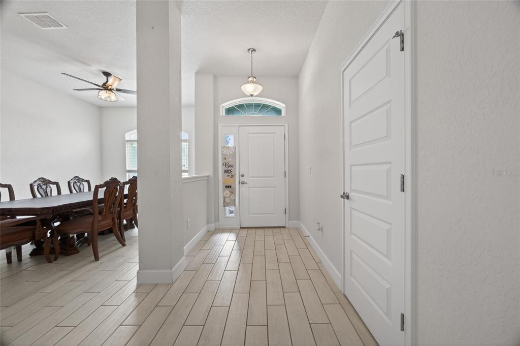 A bright entryway features light wood-look tile flooring, a white front door, and an adjacent dining area — 8356 SW 59TH TERRACE, OCALA, FL