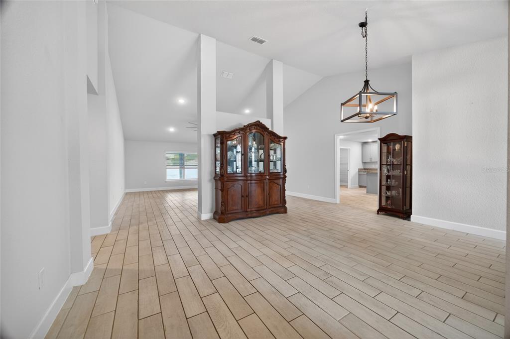 A bright, open-concept room features light wood-look tile flooring, vaulted ceilings, and two wooden cabinets — 8356 SW 59TH TERRACE, OCALA, FL